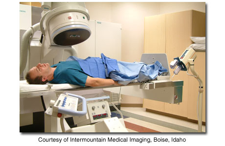 Person lying under X-ray machine in cath lab.