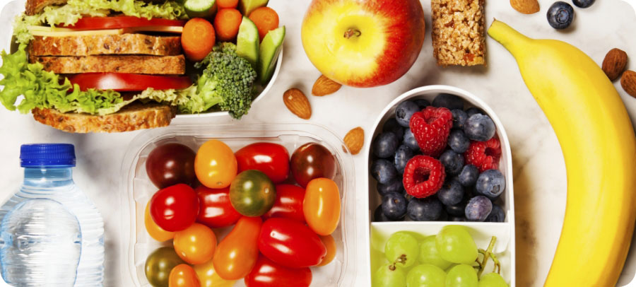 Sandwich, veggies, apple, nuts, tomatoes, fruit on a table.