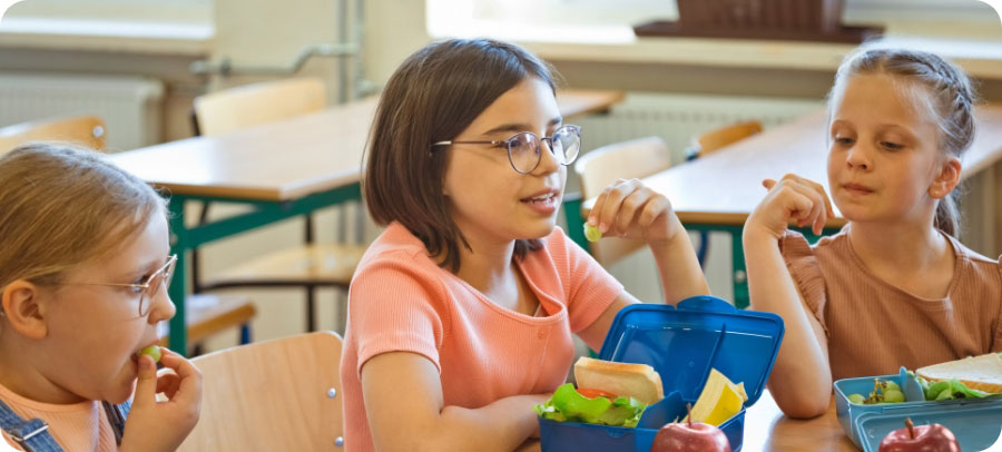 Three kids at a lunch table eating healthy food.