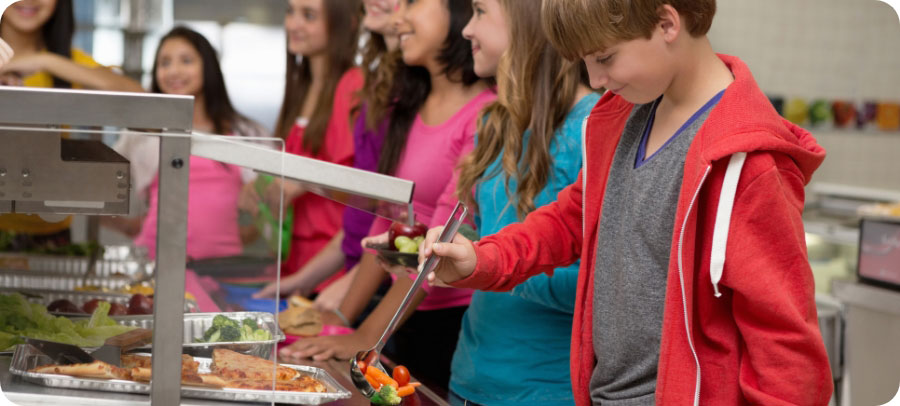 Kids in line at cafeteria putting food on their trays.
