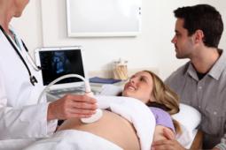 mom and dad to be watching screen as doctor performs ultrasound