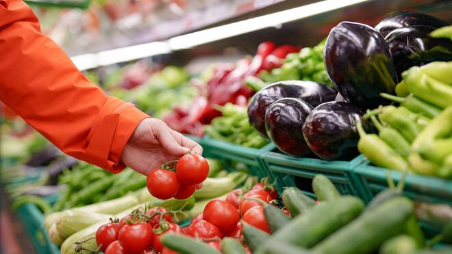 Person selecting tomatoes from produce case at grocery store
