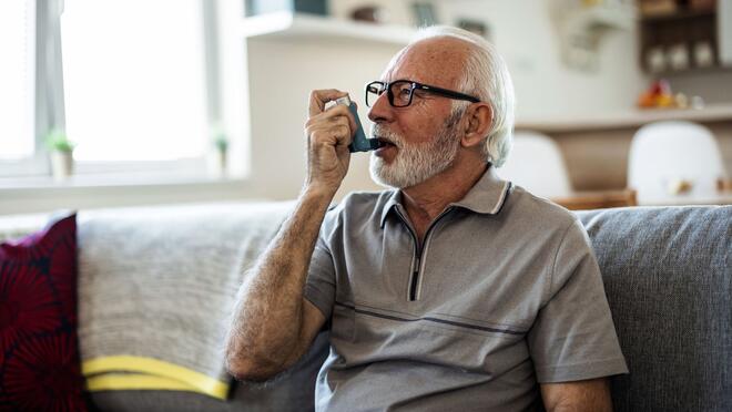 Older person sitting on sofa using an inhaler