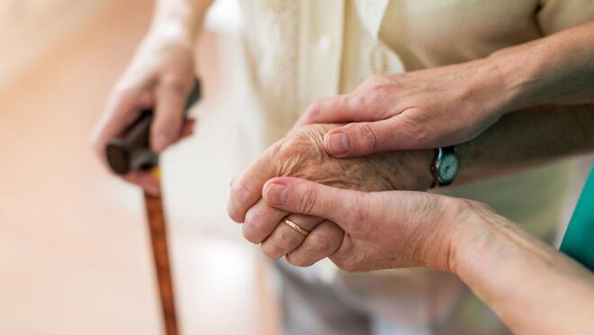 Health worker holding hand of older person with cane