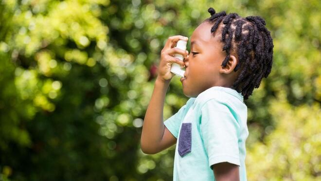 Child standing outdoors using an inhaler