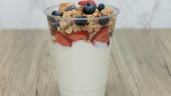 A cup of yogurt with fruit and cereal toppings