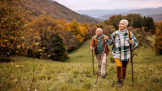 Two older adults hiking with autumnal foliage backdrop