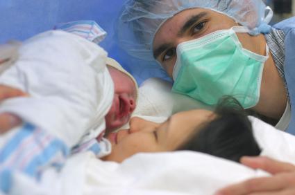 mom with newborn baby, dad at side of bed wearing hospital mask