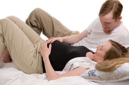 preganat woman lying on back holding stomach, man touching her stomach