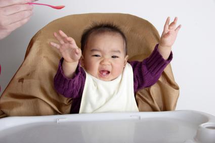 baby in high chair waving arms in the air, about to be fed with a spoon