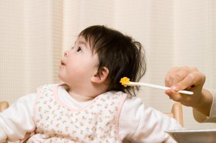 Baby looking away while mother attempts to feed her with a spoon
