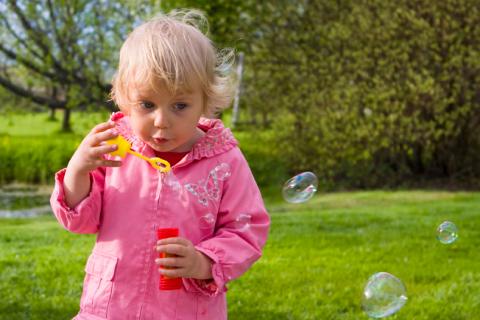toddler girl playing outside blowing bubbles