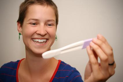 woman smiling, looking at a pregnancy test