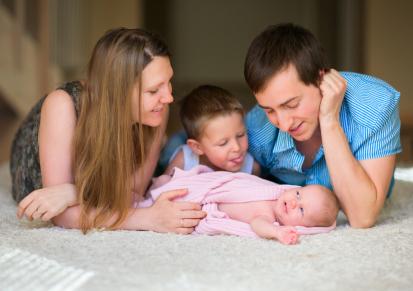 mom, boy and dad play with new baby on floor