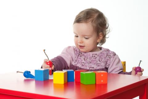 toddler playing with blocks and tops on table