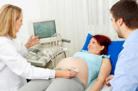 pregnant woman on bed getting ultrasound exam with doctor, partner watching