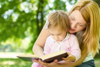 mom holding toddler girl and reading book to her
