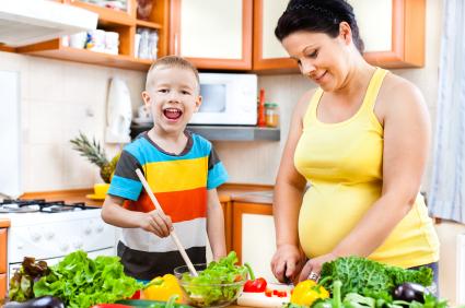 pregnant woman with boy chopping vegatables and making salad