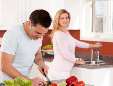 pregnant woman washing food in sink, man chopping vegatables