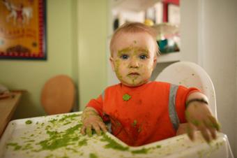baby in high chair covered with green food
