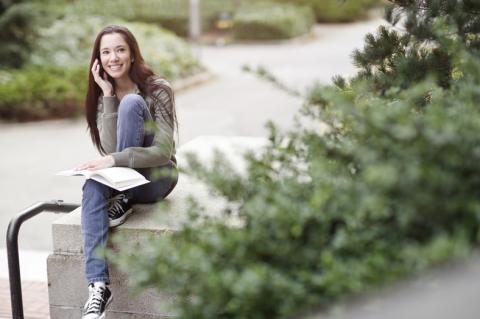 teenager with book talking on phone outdoors