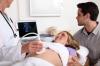 mom and dad to be watching screen as doctor performs ultrasound